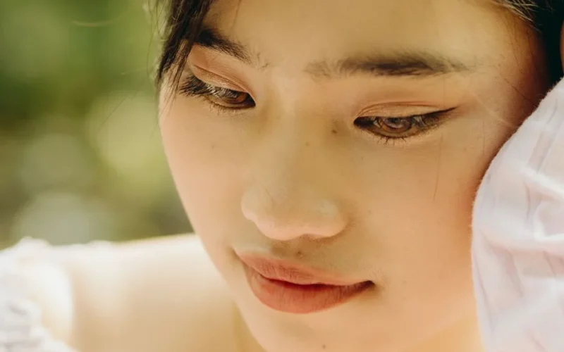 Serene close-up portrait of a young woman with natural makeup, outdoors.
