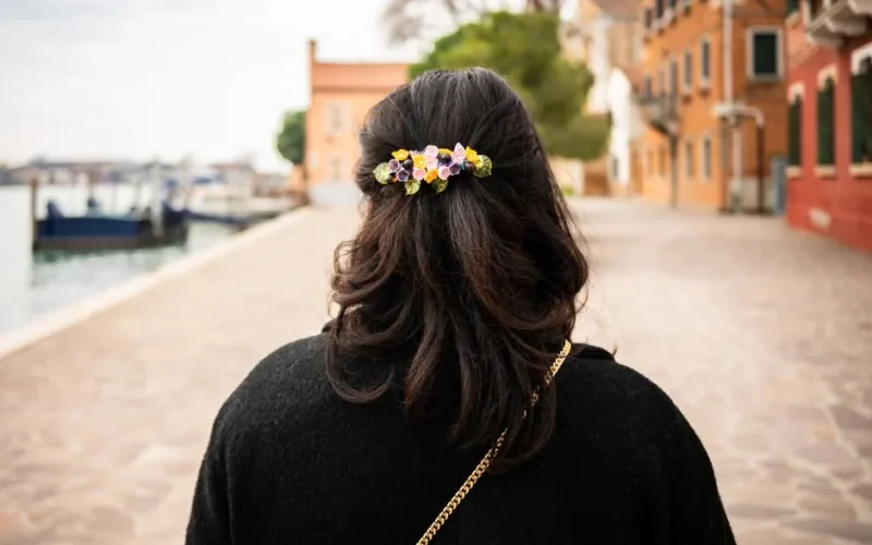 Rear view of a woman with floral hair accessory walking along a canal in Venice.