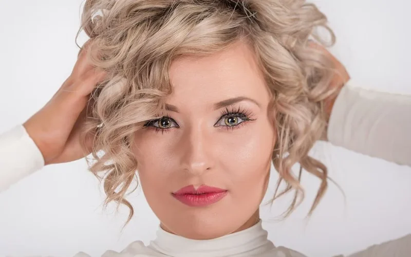 Close-up portrait of a blonde woman with curly hair and makeup, embracing elegance.