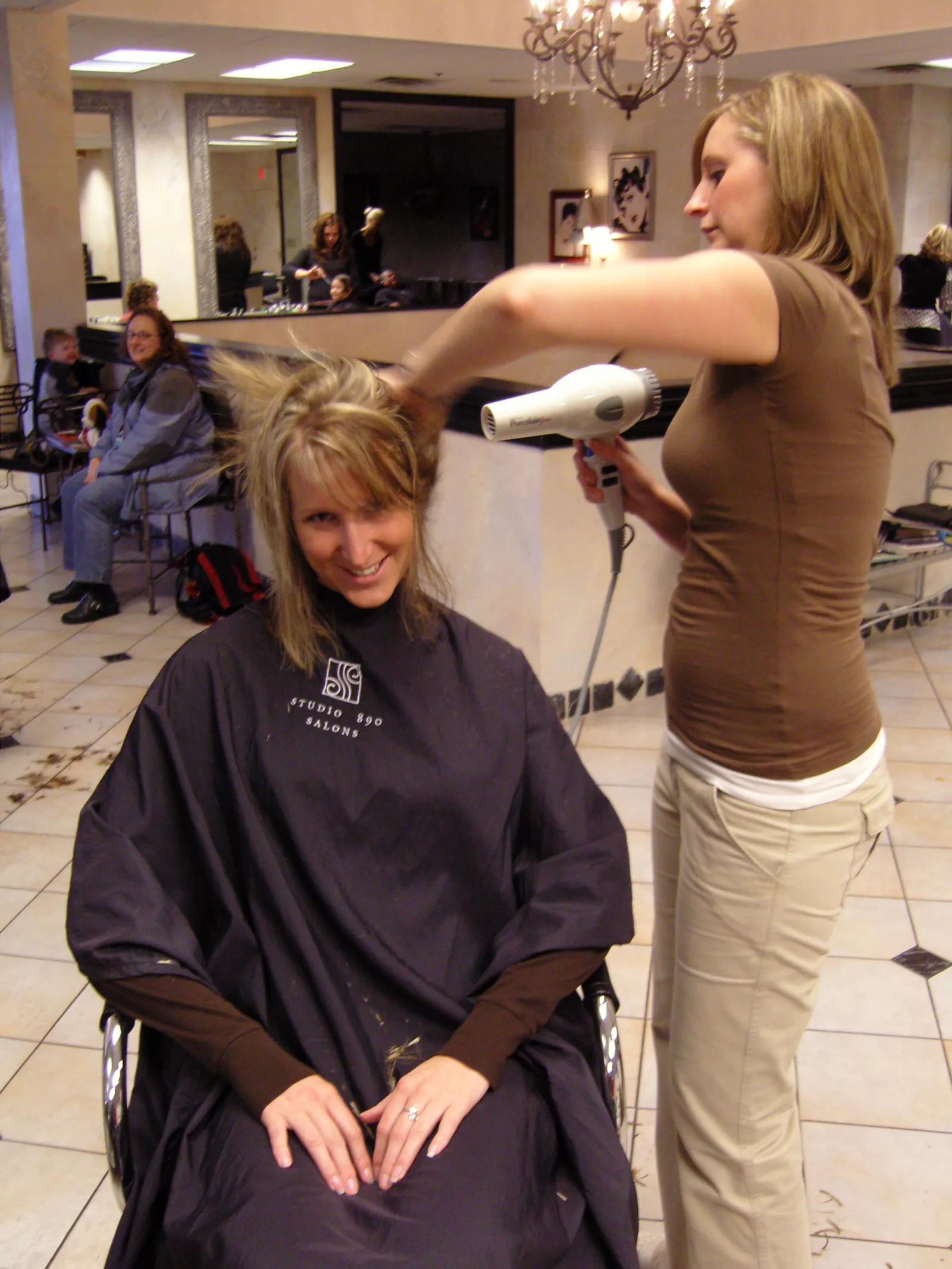 Woman in a salon drying another's blonde hair with a hair dryer.
