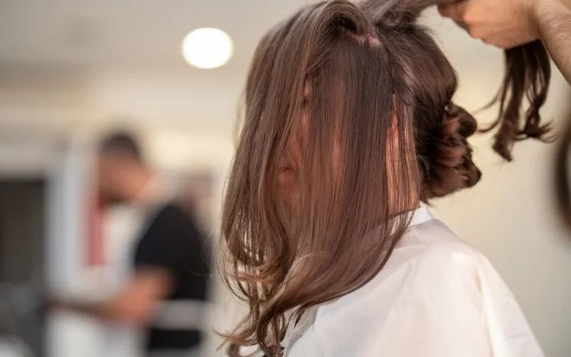 Side view of a woman getting hair styled by hairstylist in a modern salon setting.