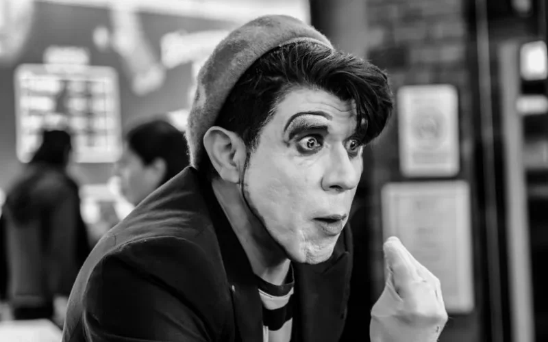 A captivating black and white portrait of a mime artist performing indoors, showcasing expressive facial expressions and makeup.