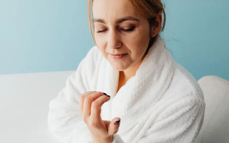 Adult woman in a bathrobe admiring her newly manicured nails, embracing a moment of self-care.