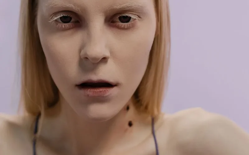 Close-up portrait of a woman with vampire makeup against a purple background, exuding a haunting and eerie vibe.