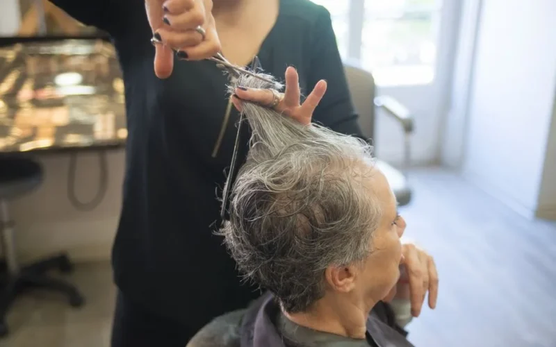 A hairdresser styles a senior woman's hair in an indoor salon setting.
