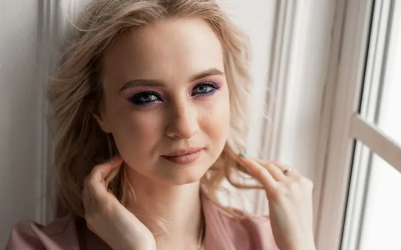 Close-up portrait of a young woman with glamorous purple eye shadow and elegant hairstyle.