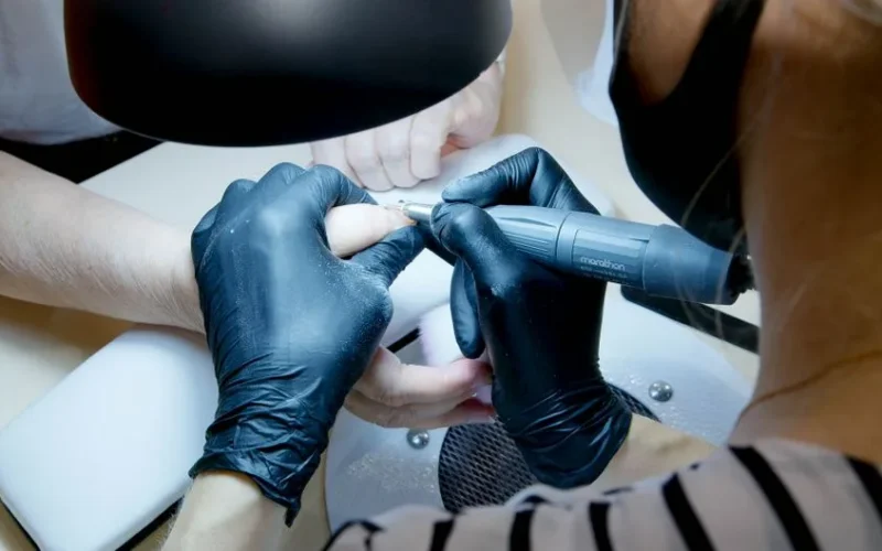 Close-up of manicurist using tool on client's nails in salon setting.