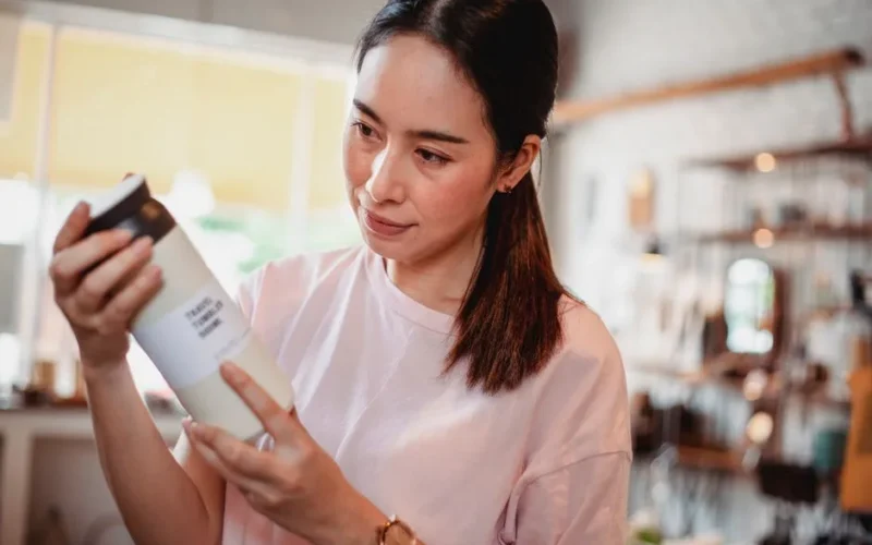 Crop young attentive ethnic shopper reading information on bottle of cosmetic product in store