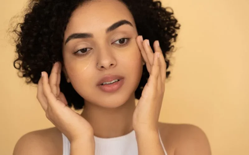 Close-up of a woman applying under-eye mask in a studio setting, focusing on skincare and wellness.