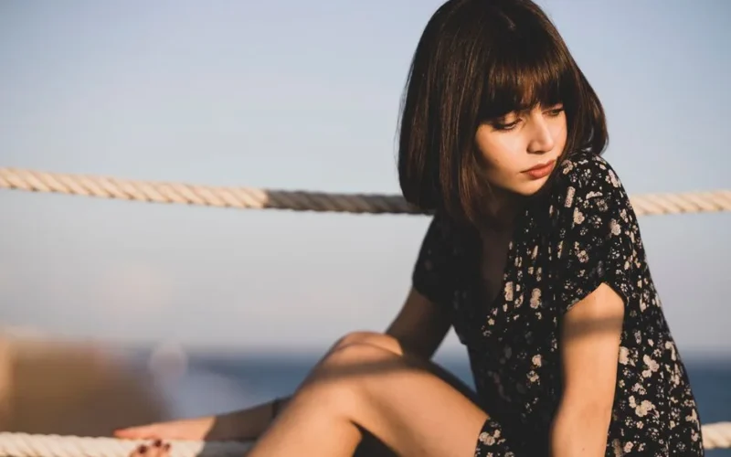 Portrait of a woman with bangs sitting by a rope outdoors, enjoying a sunny day.