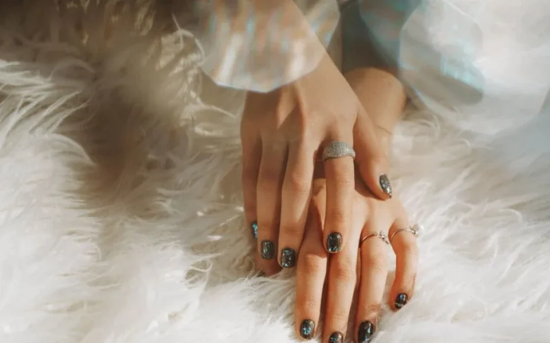 Close-up of a woman's hands wearing rings and nail art, resting on white faux fur.