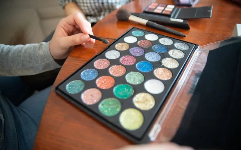 Vibrant glitter eyeshadows with makeup brushes on wooden table. Perfect for beauty and fashion themes.