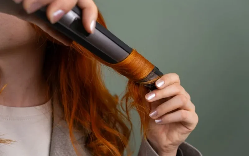 Close-up of a woman curling her vibrant red hair with a curling iron.