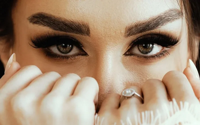 Intense close-up photography of a woman's eyes with striking makeup and elegant ring.