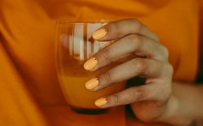 Crop anonymous female in yellow t shirt with trendy nail art holding glass of freshly squeezed cold orange juice