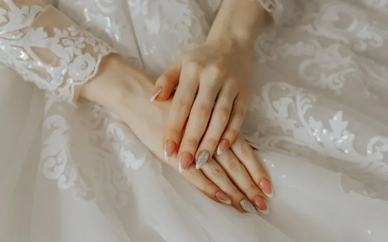 Close-up of a bride's hands on a detailed lace wedding dress, highlighting elegance and beauty.