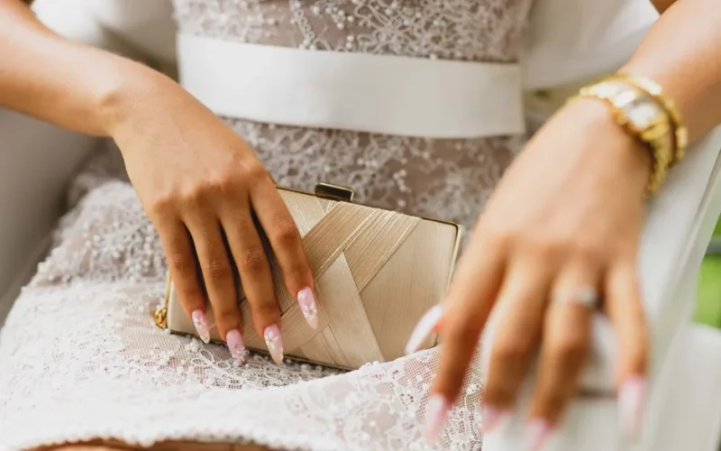 Bride in lace dress holding clutch, showcasing elegant wedding accessories.