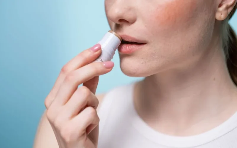 A woman applying lip balm to her lips, highlighting skincare and self-care routine.