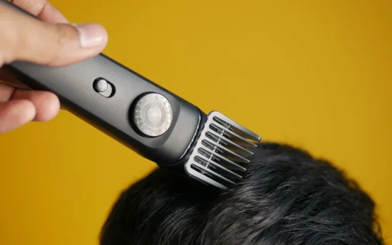 Close-up of an electric hair clipper trimming hair against yellow background.