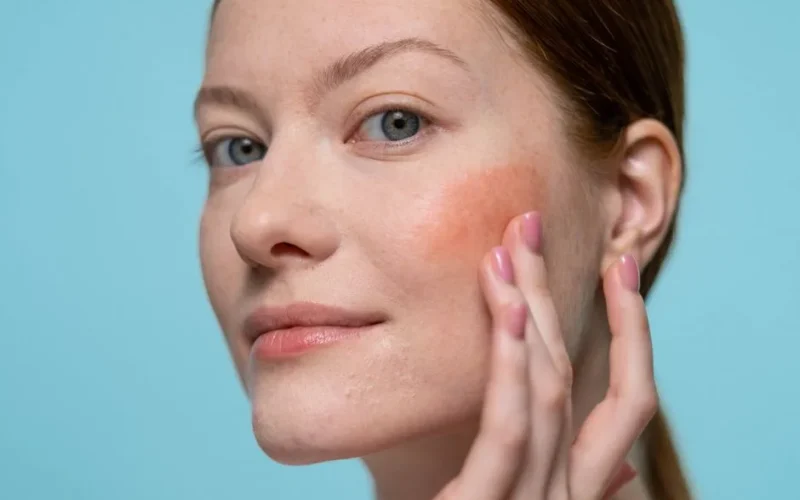 Woman applying blush on her face, highlighting healthy skin and beauty in a studio setting.