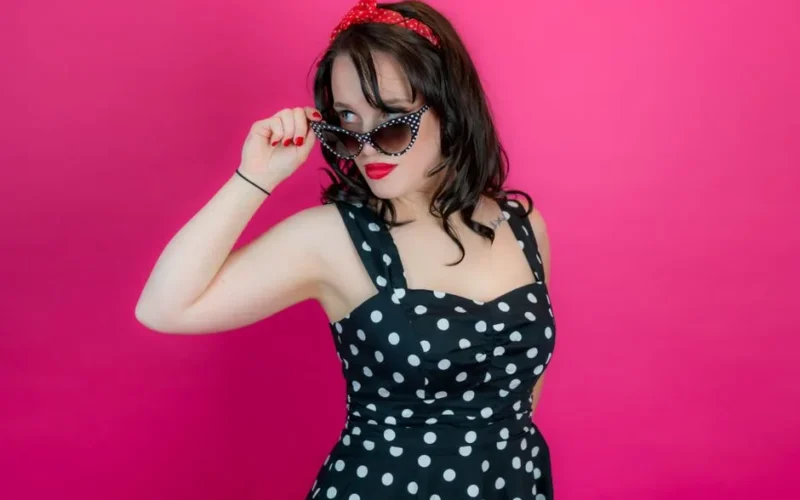 Stylish woman in polka dot dress and sunglasses embodying classic pin-up style with bold red lips.