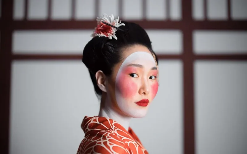 Portrait of a traditional geisha in elegant red kimono with striking makeup.