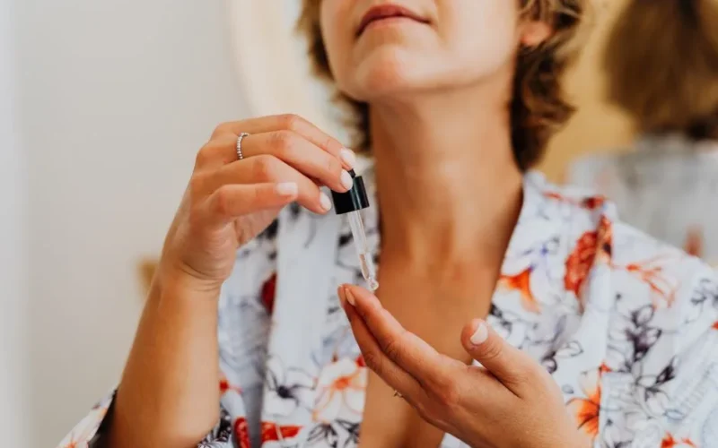 Close-up of a woman in a floral robe applying facial serum using a dropper.