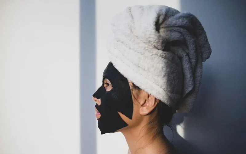 Woman wearing a black facial mask and towel turban, side profile in natural lighting.