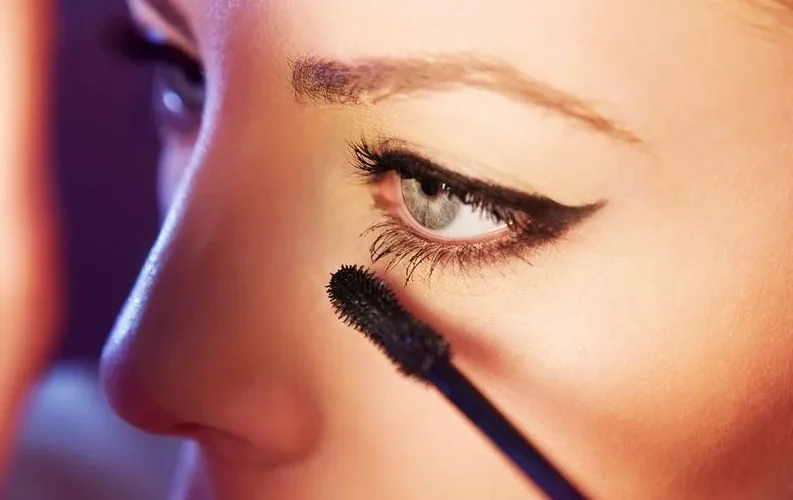 Detailed close-up of a woman applying mascara to her eyelashes, highlighting eye makeup.