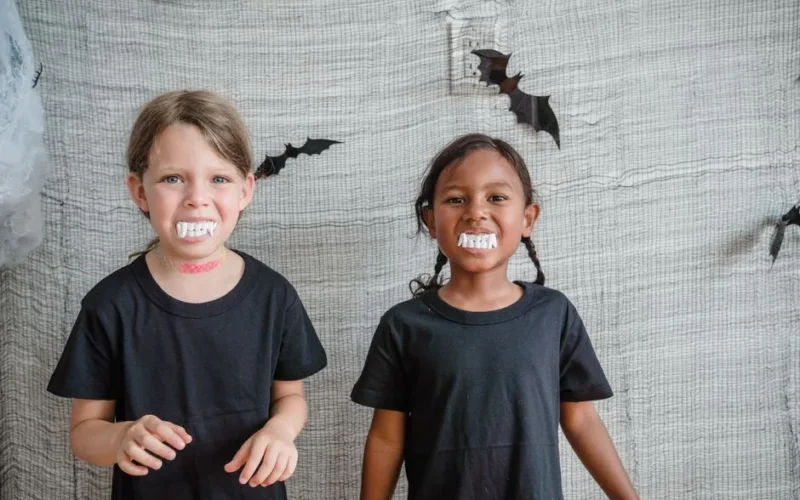 Two children wearing vampire costumes with fake teeth having fun indoors on Halloween.