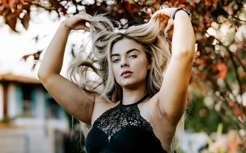 Blonde woman in lace top posing with autumn leaves outdoors.