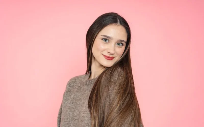 Portrait of a smiling young woman with long brown hair against a pink background.