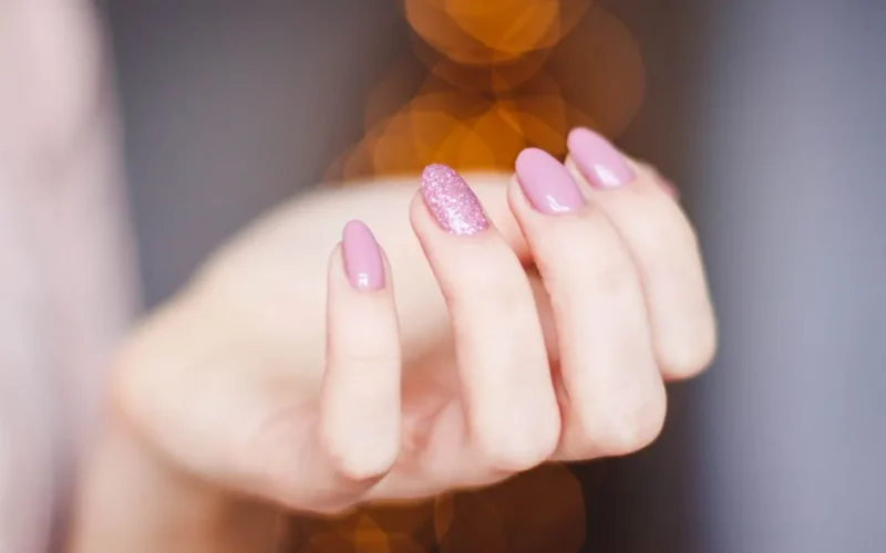 A close-up of a woman's hand displaying a stylish pink glitter manicure, highlighting nail art details.