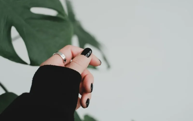 Close-up of a hand with black manicured nails and a silver ring against a green leaf background.
