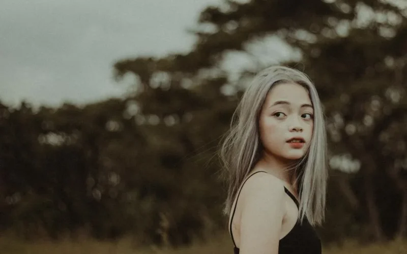 Portrait of young Asian woman with silver hair glancing over shoulder, outdoors.