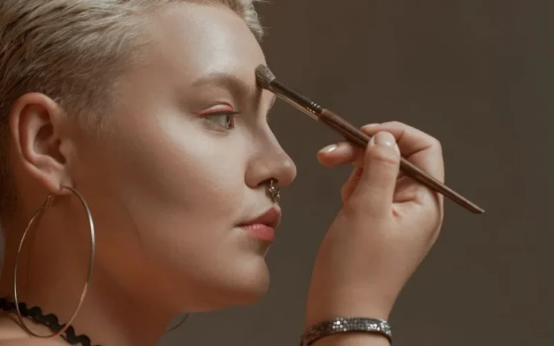 Close-up of a woman applying makeup with a brush, featuring jewelry and a stylish look.