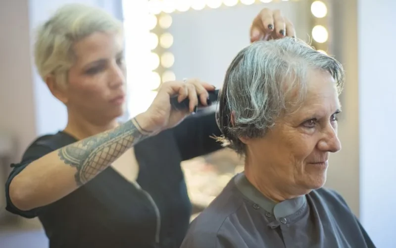 A hair stylist trims the hair of a smiling senior woman in a salon.