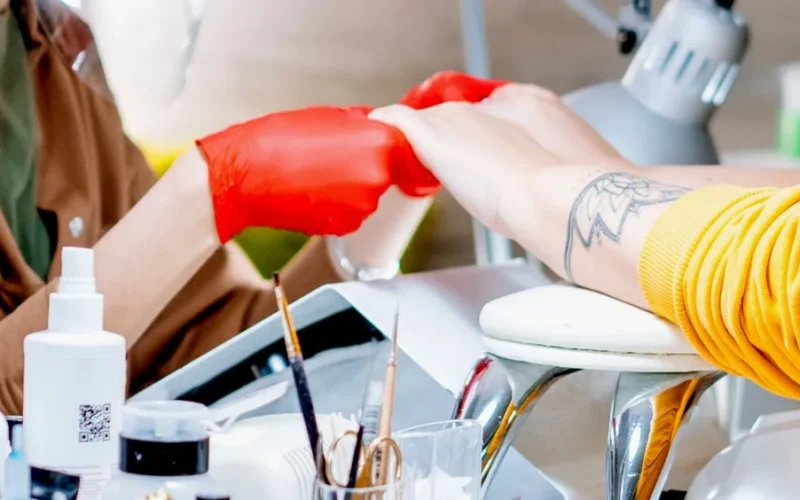 Crop anonymous master of nail salon in red gloves holding hands of unrecognizable client