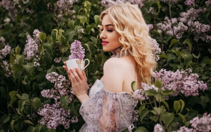 Elegant portrait of a woman in a floral scene holding lilacs, capturing spring beauty.