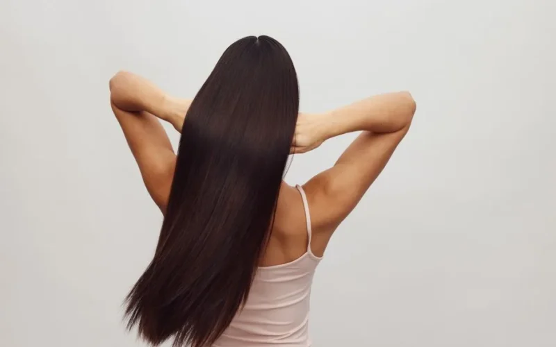 Asian woman with long, straight hair shown from behind, embracing hair care and beauty.