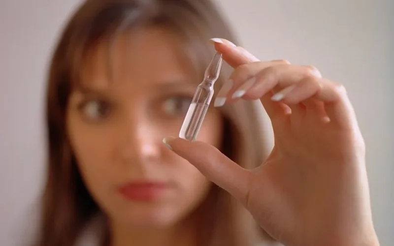 Focused woman examining glass ampoule of liquid with blurred background.