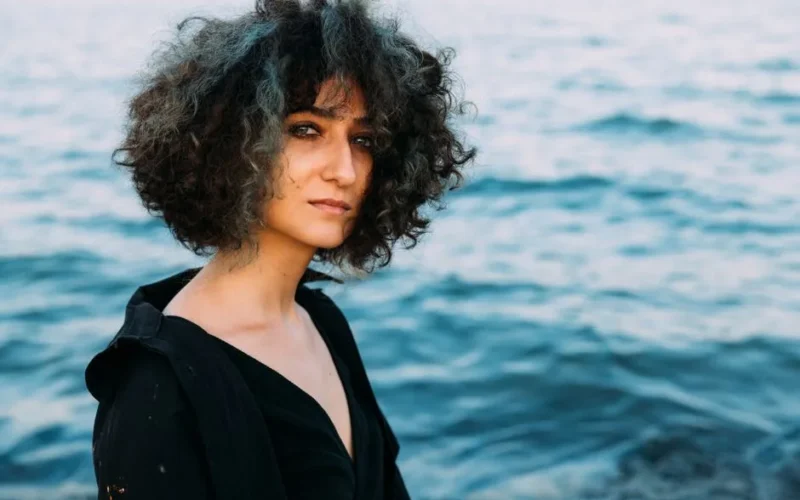 Portrait of a young woman with curly hair by the sea, exuding natural beauty and authenticity.