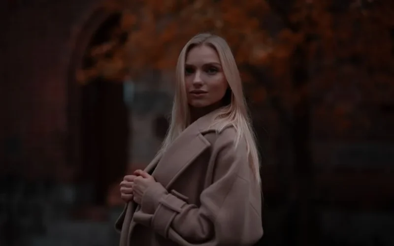 Stylish woman in a coat posing outdoors with autumn foliage in Berlin.