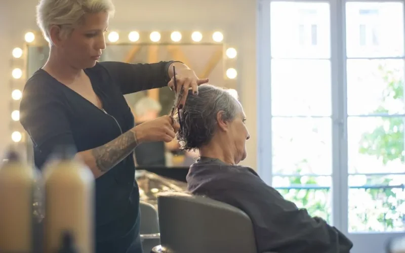 Hairdresser expertly trims senior client's hair in well-lit salon setting, focusing on precision.