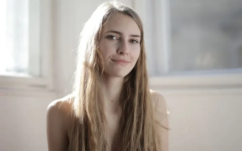 Portrait of a smiling young woman with long blonde hair indoors. Natural lighting creates a warm ambiance.