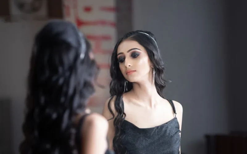 Beautiful woman in black dress gazing at her reflection in a mirror.