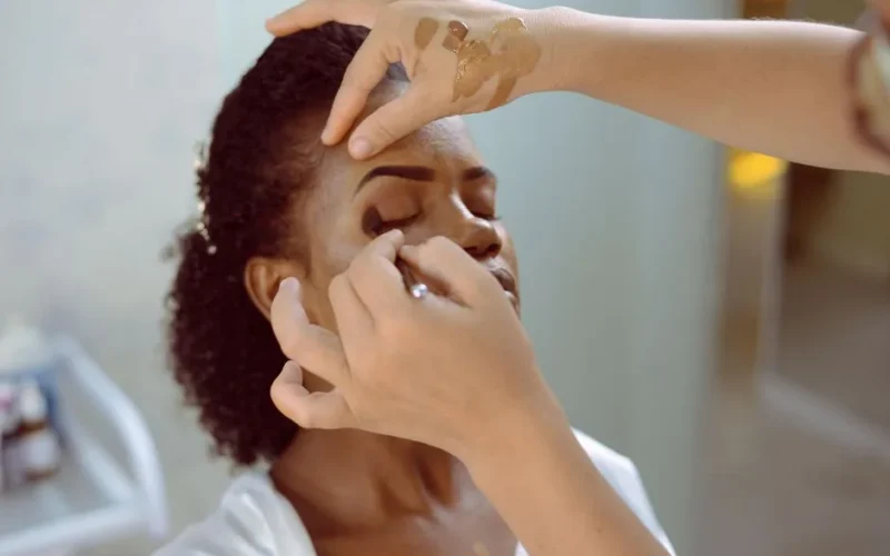 Close-up shot of a makeup artist applying eyeshadow on a black woman.
