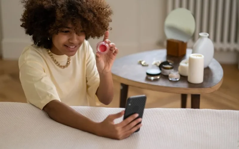 Young woman recording a video review of beauty products using a smartphone indoors.