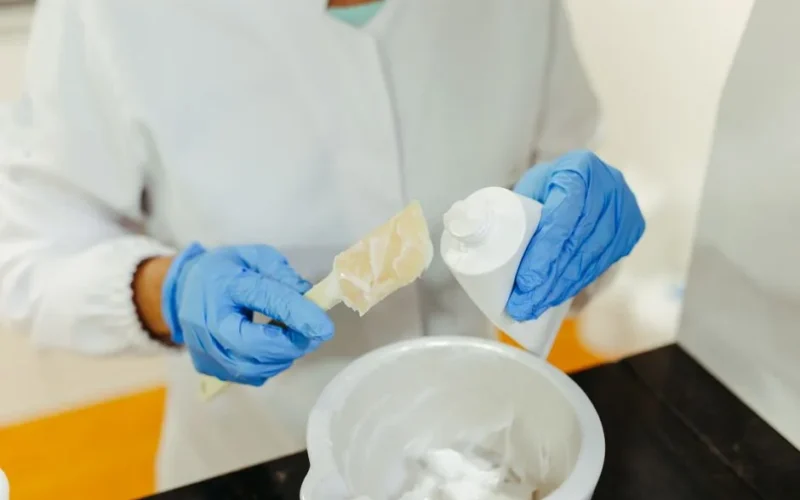A lab technician wearing gloves mixes skincare cream with precision for research purposes.