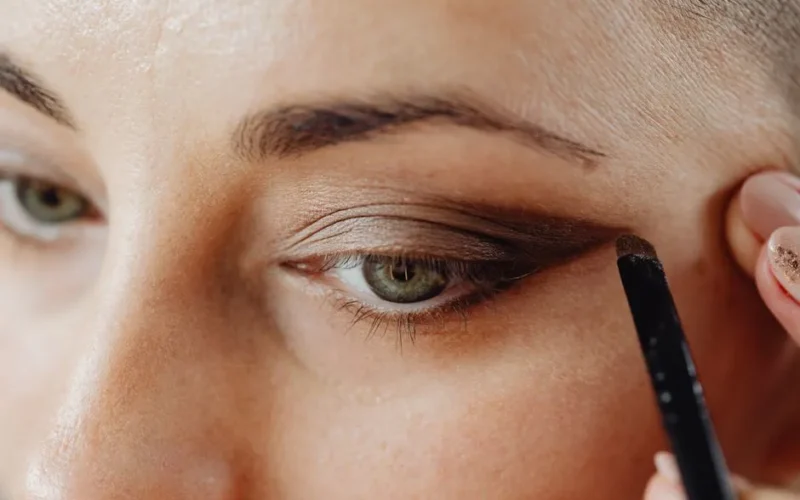 A detailed close-up of a woman applying eyeshadow using a makeup brush, highlighting the eye area.